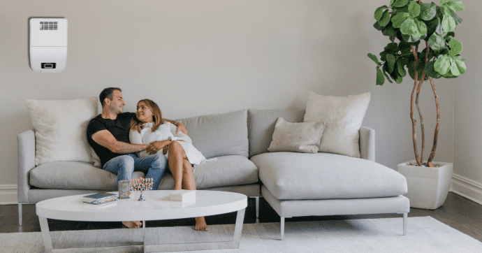 Paar sitzt auf dem Sofa, hinter ihnen befindet sich ein Luftbehandlungssystem an der Wand 