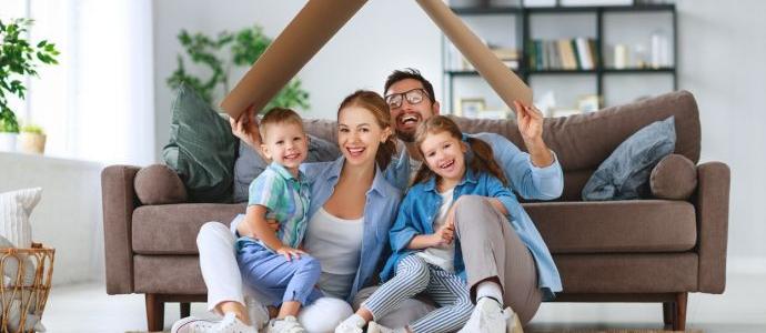 Eine glÃ¼ckliche Familie sitzt in ihrem feuchtigkeitsfreien Haus mit einem Pappdach Ã¼ber dem Kopf auf dem Boden vor dem Sofa
