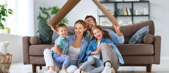  Une famille heureuse est assise par terre devant le canapé dans leur maison sans humidité, sous un toit en carton.