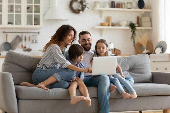 Une famille est confortablement installée dans le canapé et regarde l'écran d'un ordinateur portable