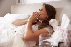 Une femme allongée dans son lit qui se mouche