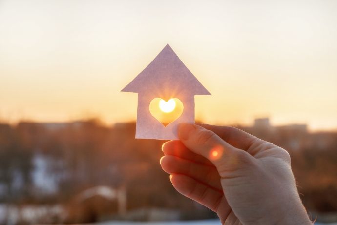 Une maison en papier avec un cœur au milieu laisse entrevoir le lever du soleil.