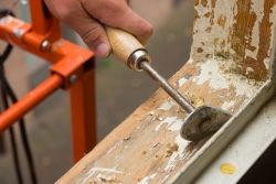 Mann entfernt Holzfäule von einem Fensterrahmen